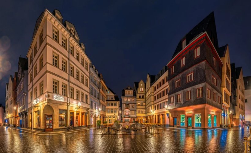 Historic buildings in Frankfurt, Germany reflect off rain-soaked streets at night.