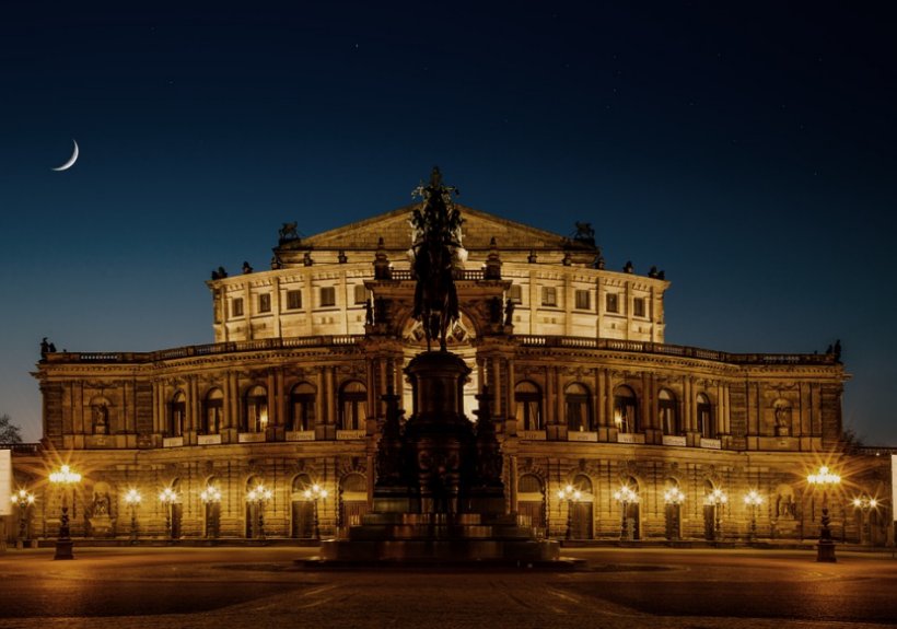 The Semperoper stands against a night sky and crescent moon in Dresden, Germany